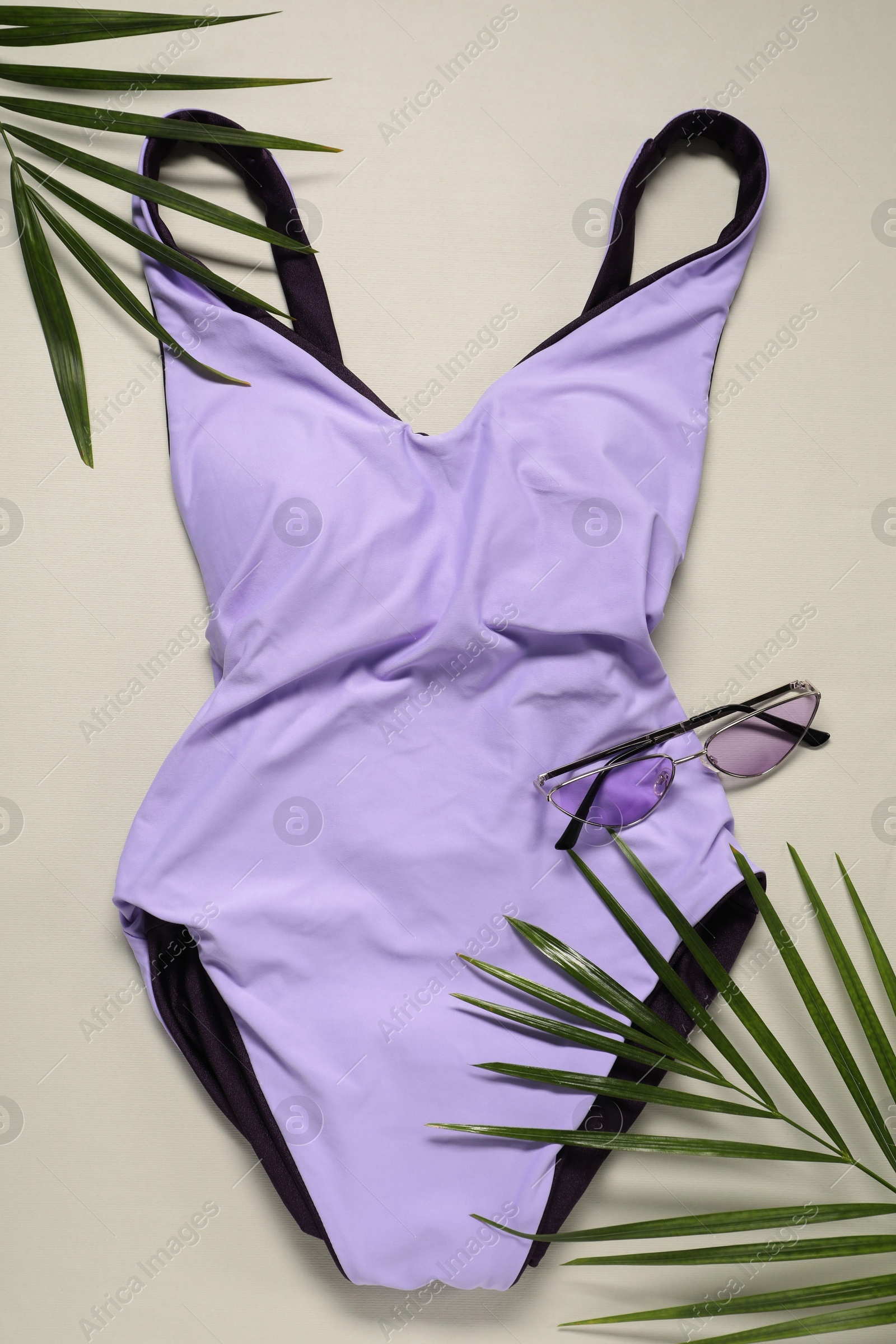 Photo of Violet swimsuit, sunglasses and palm leaves on beige background, flat lay