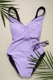 Violet swimsuit, sunglasses and palm leaves on beige background, flat lay