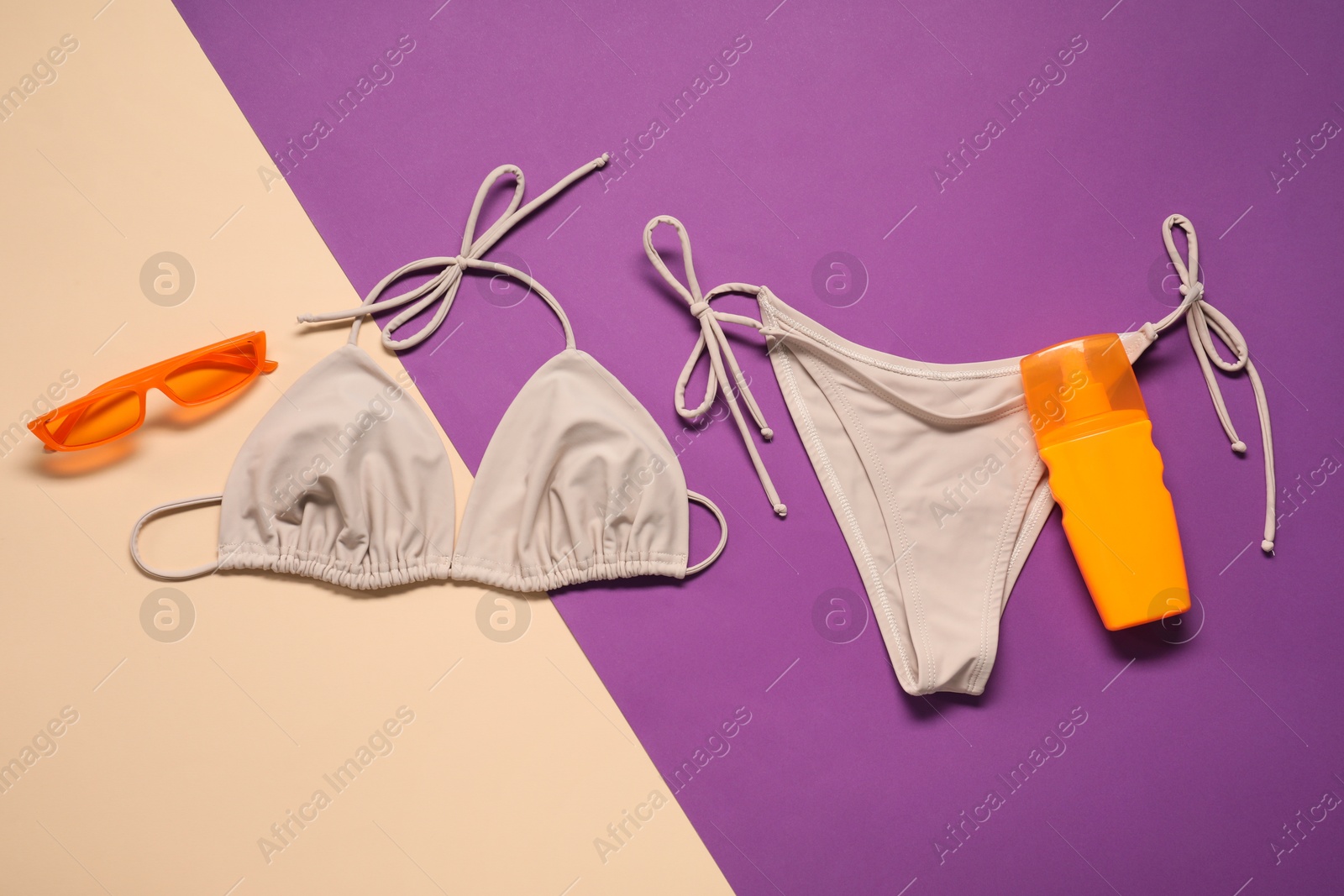 Photo of Beige swimsuit, sunglasses and sunscreen on color background, flat lay