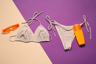 Beige swimsuit, sunglasses and sunscreen on color background, flat lay