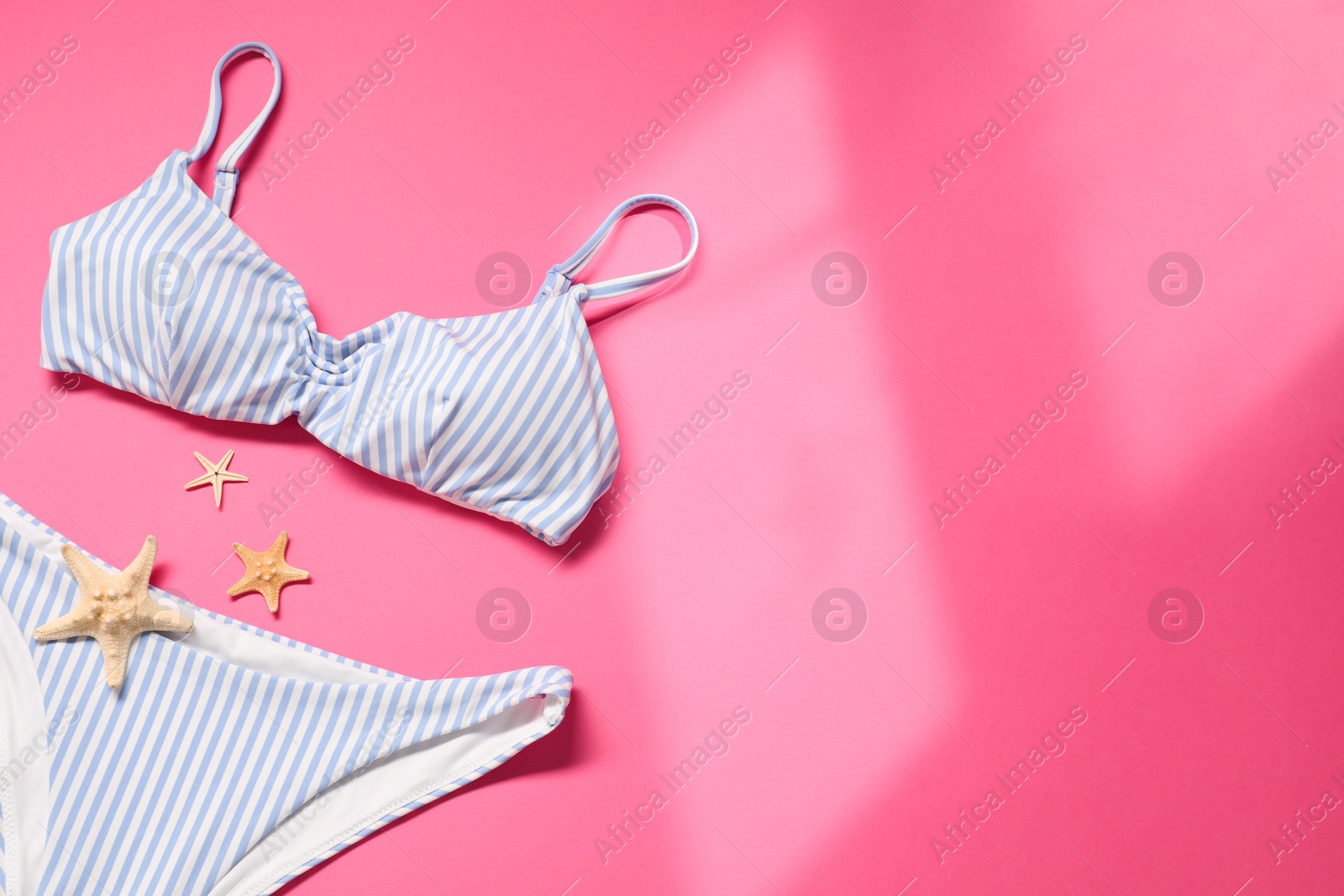 Photo of Striped swimsuit and starfishes on pink background, flat lay. Space for text