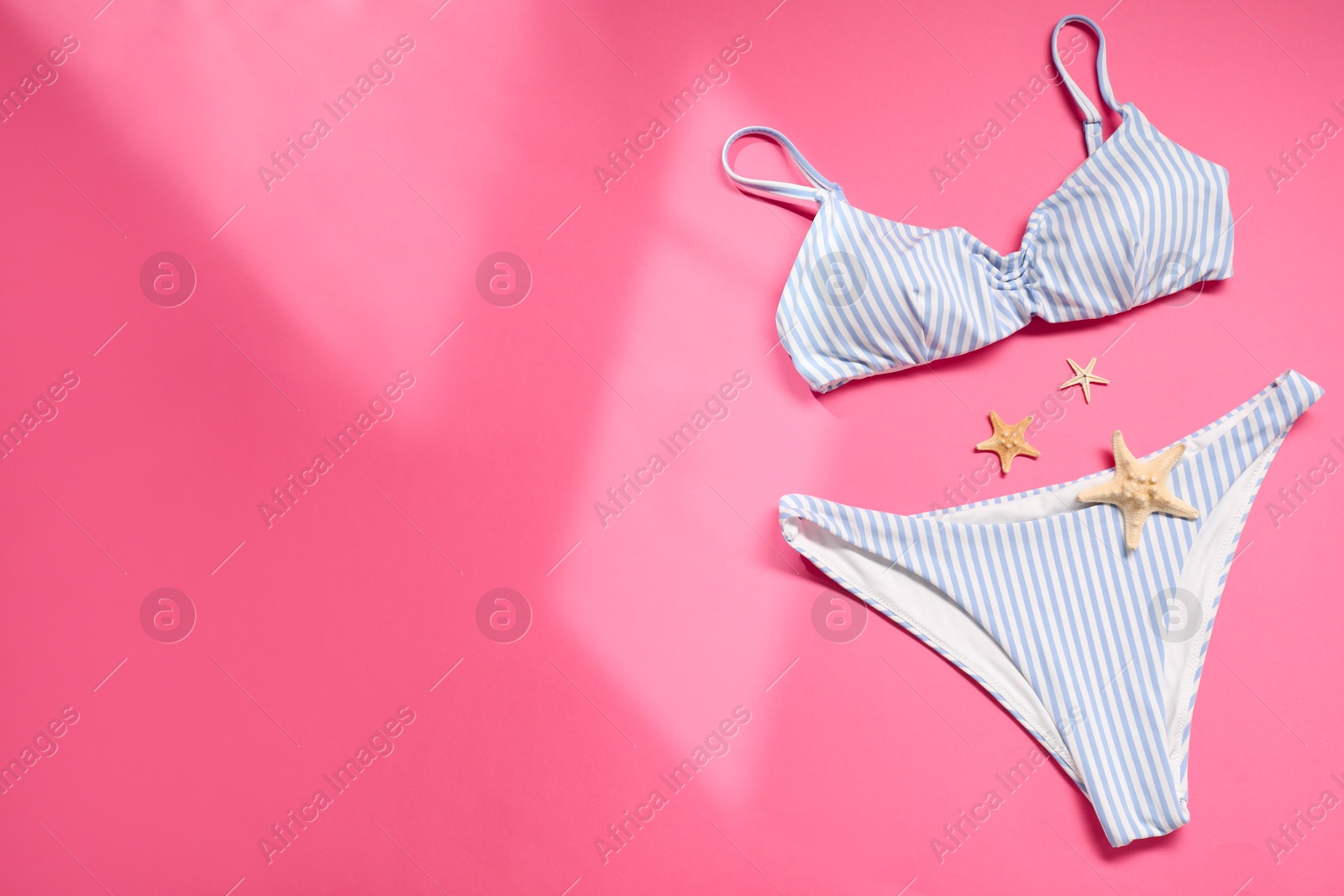 Photo of Striped swimsuit and starfishes on pink background, flat lay. Space for text