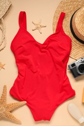 Red swimsuit, hat, sunscreen and camera on beige background, flat lay