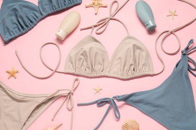 Photo of Beautiful swimsuits, seashells and sunscreens on pink background, flat lay