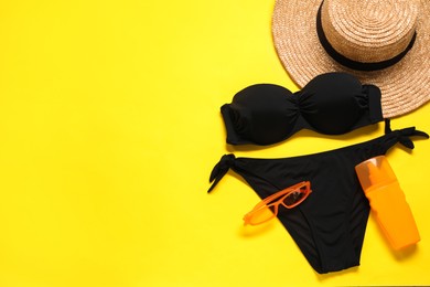 Black swimsuit, hat, sunscreen and sunglasses on yellow background, flat lay. Space for text