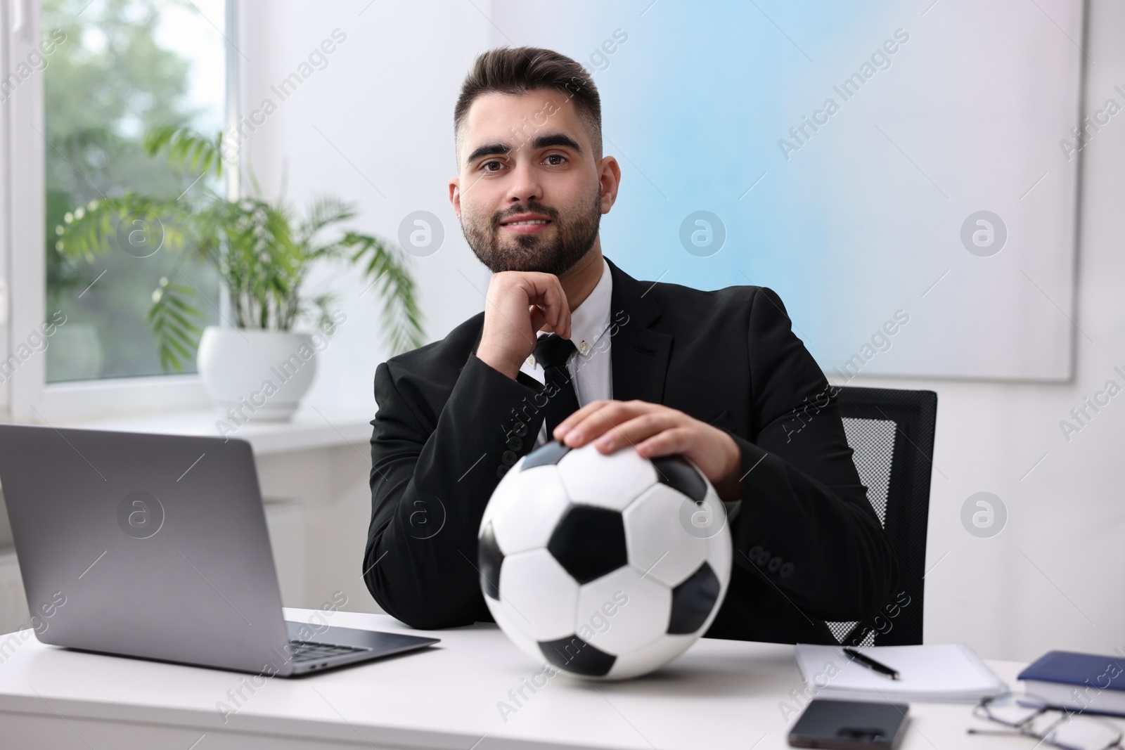 Photo of Young man with soccer ball at table in office