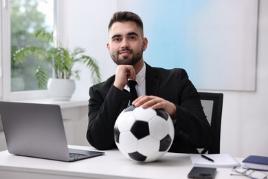 Young man with soccer ball at table in office