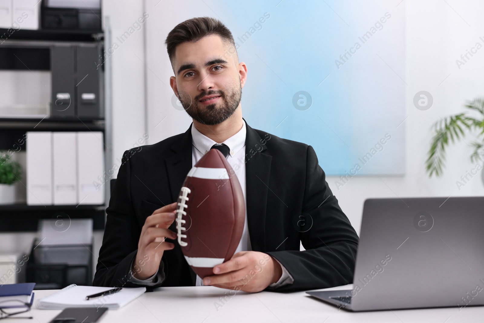 Photo of Young man with american football ball at table in office