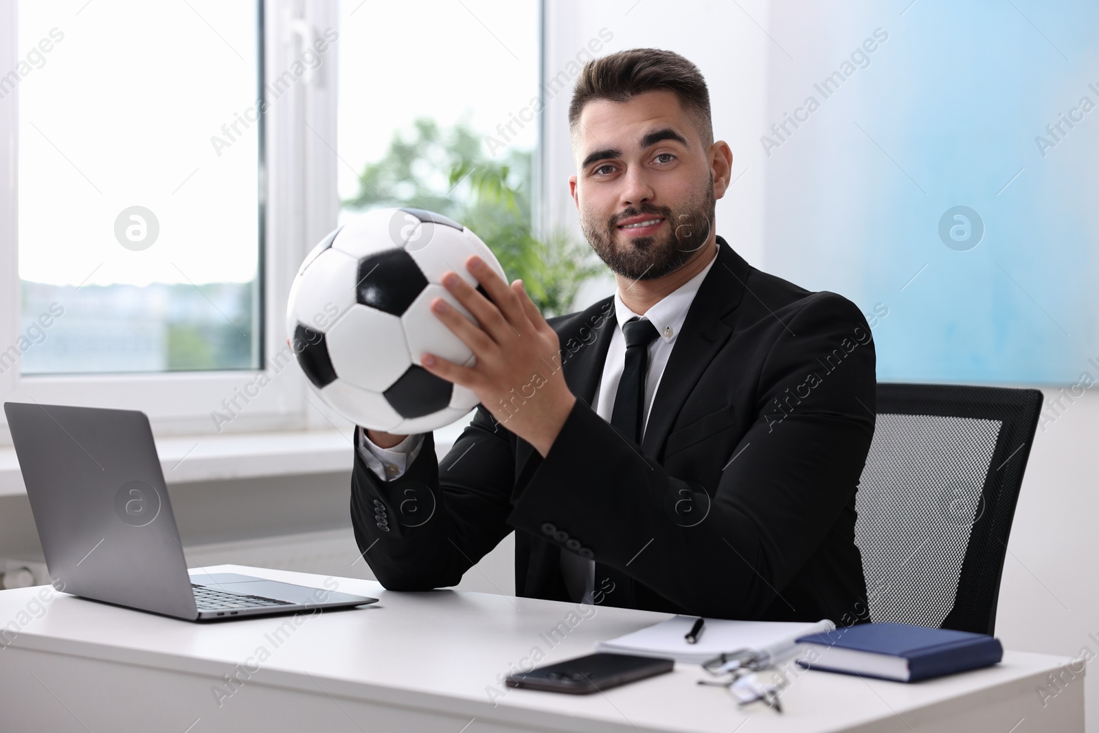 Photo of Young man with soccer ball at table in office