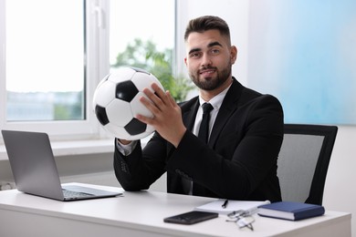 Young man with soccer ball at table in office