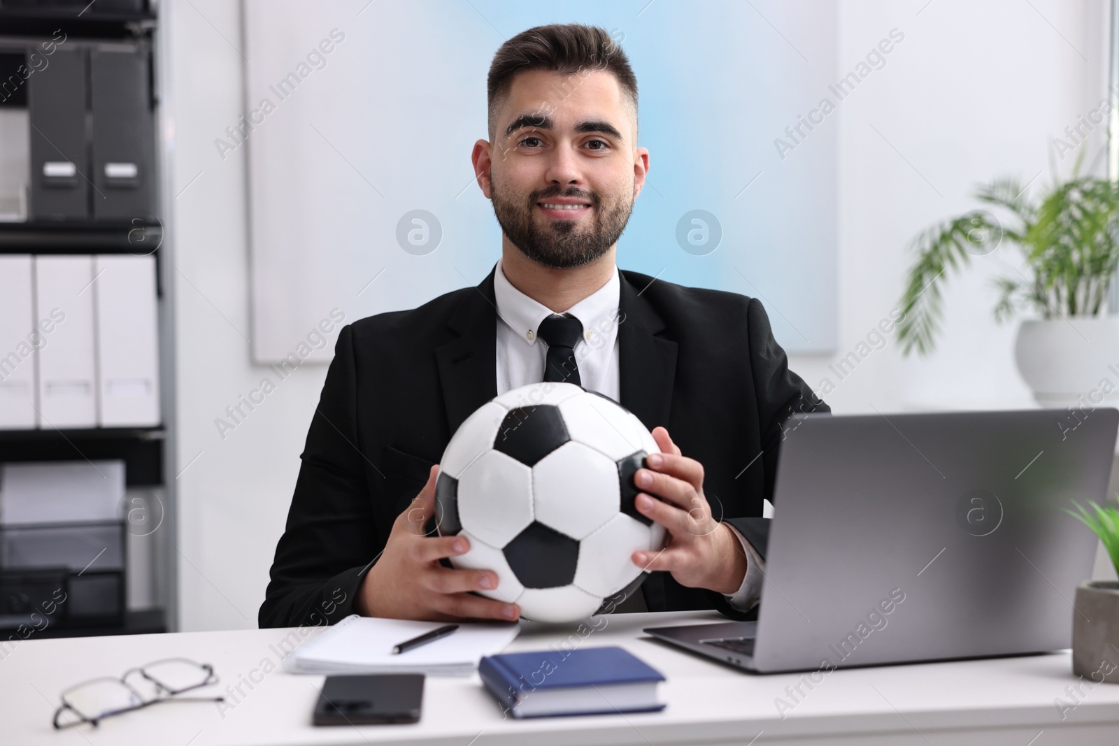 Photo of Young man with soccer ball at table in office