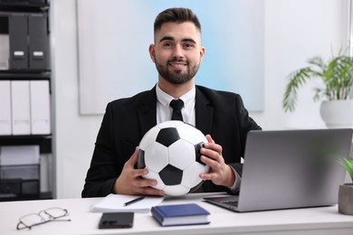 Young man with soccer ball at table in office