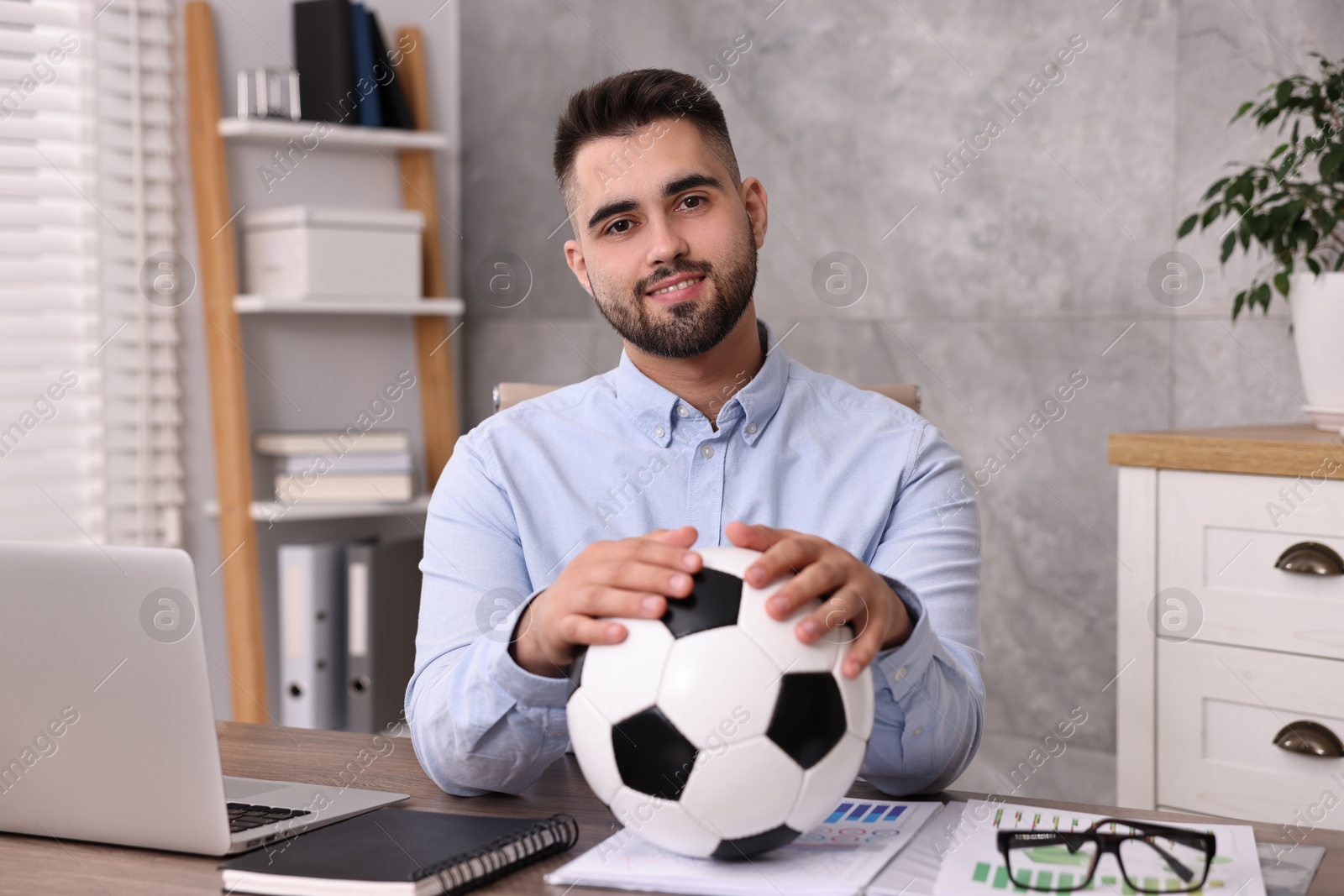 Photo of Young man with soccer ball at table in office