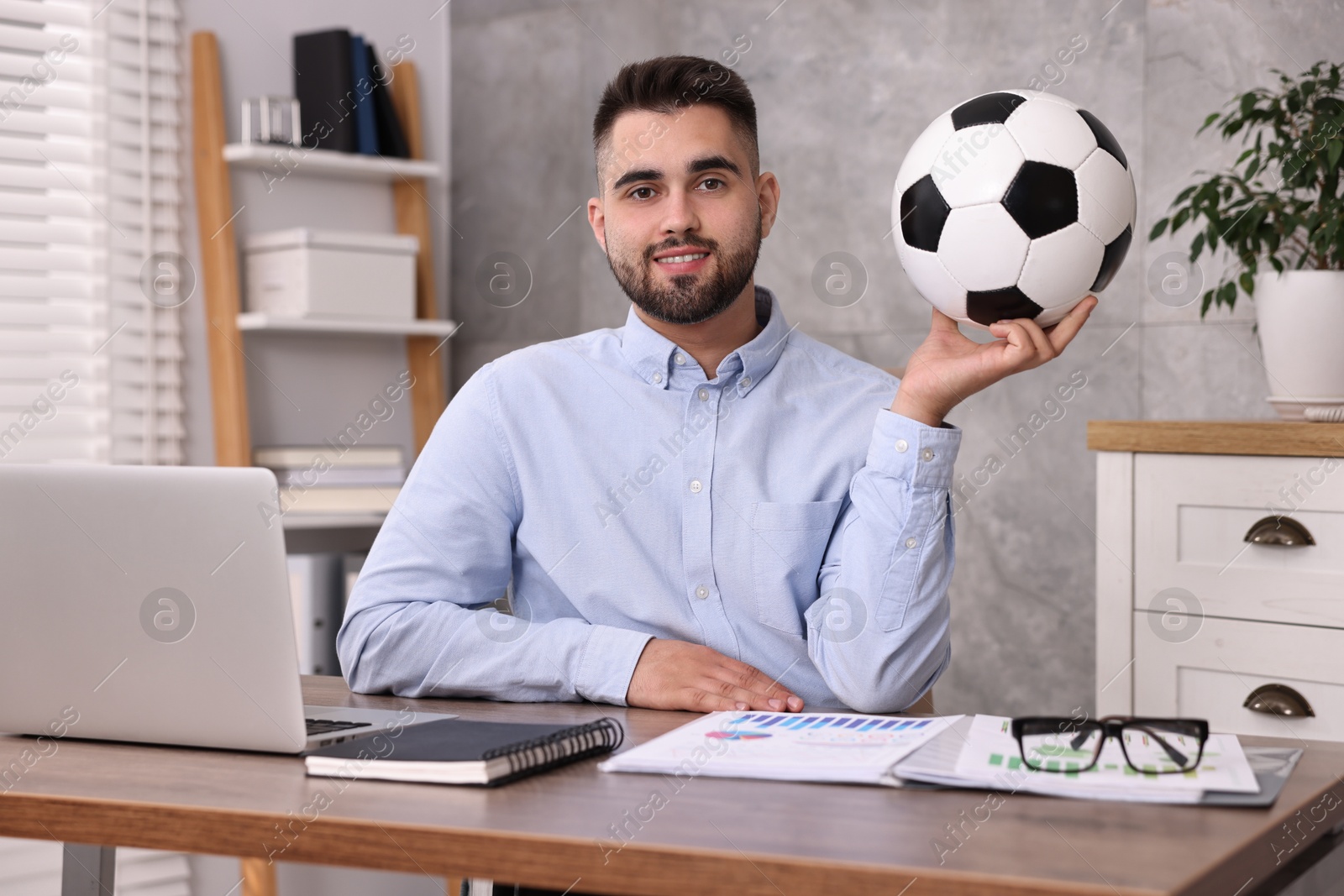 Photo of Young man with soccer ball at table in office