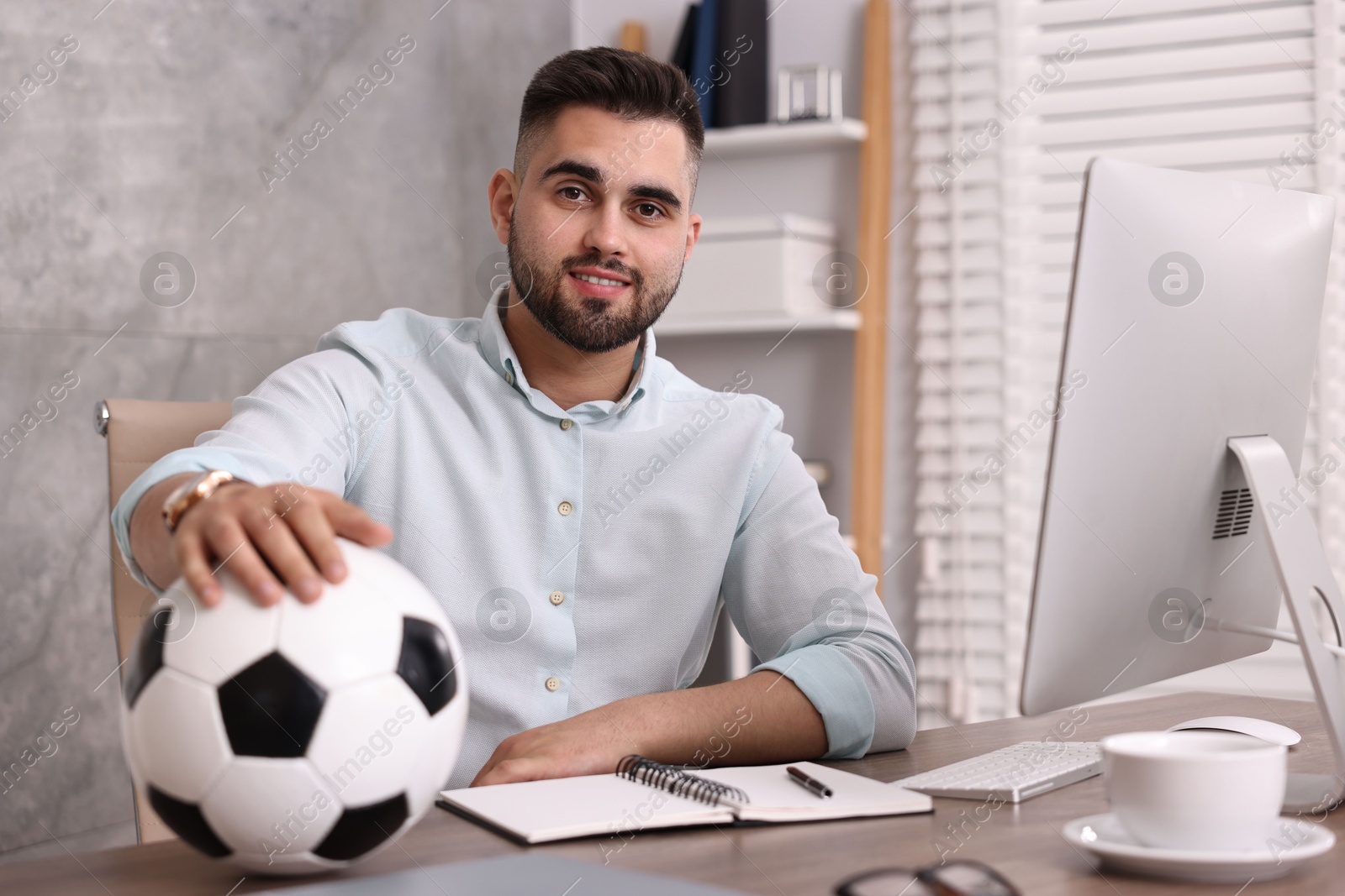 Photo of Young man with soccer ball at table in office