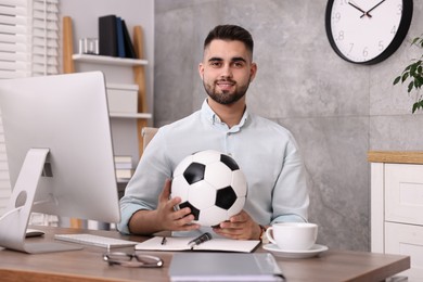 Young man with soccer ball at table in office