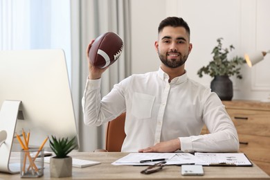 Young man with american football ball at table in office