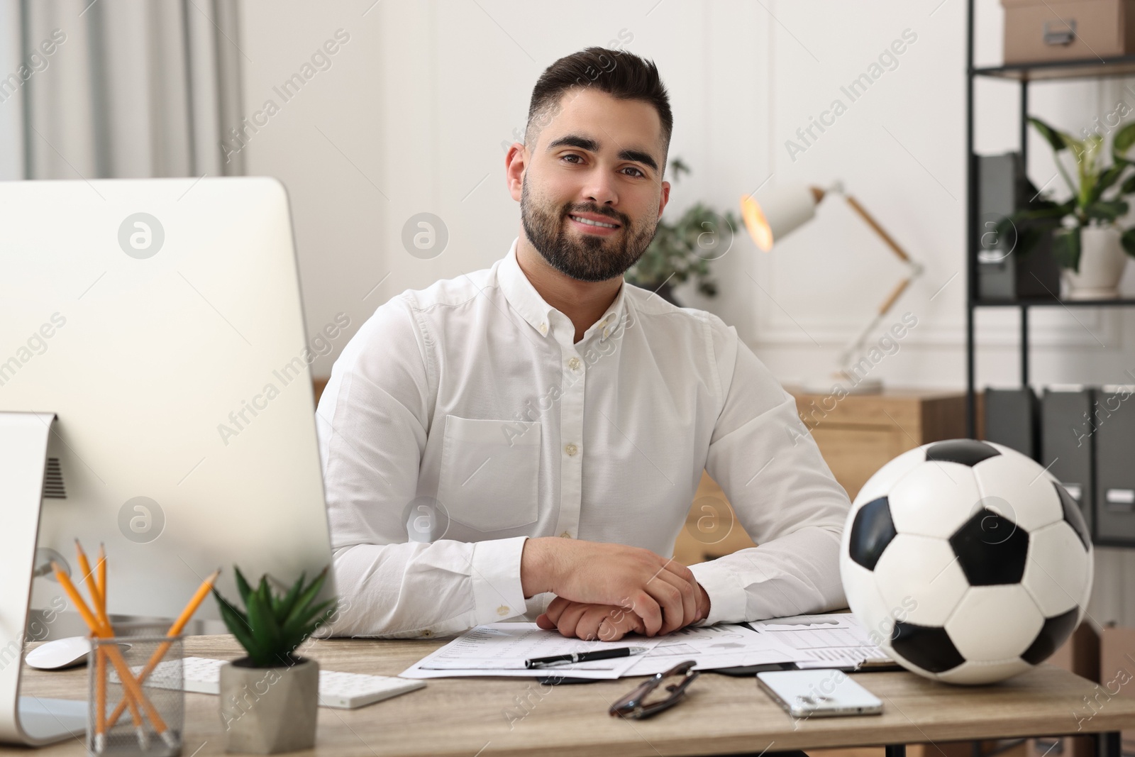 Photo of Young man with soccer ball at table in office