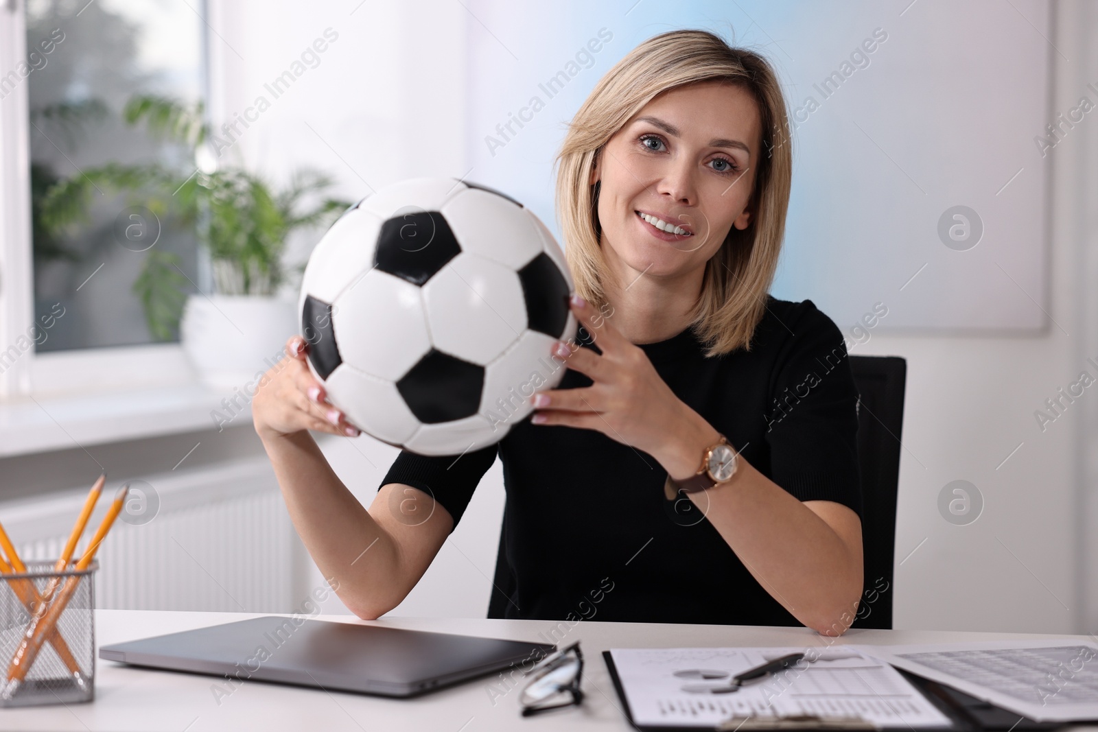 Photo of Smiling woman with soccer ball at table in office