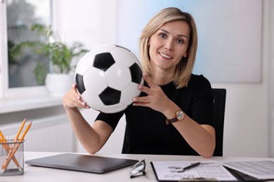 Smiling woman with soccer ball at table in office