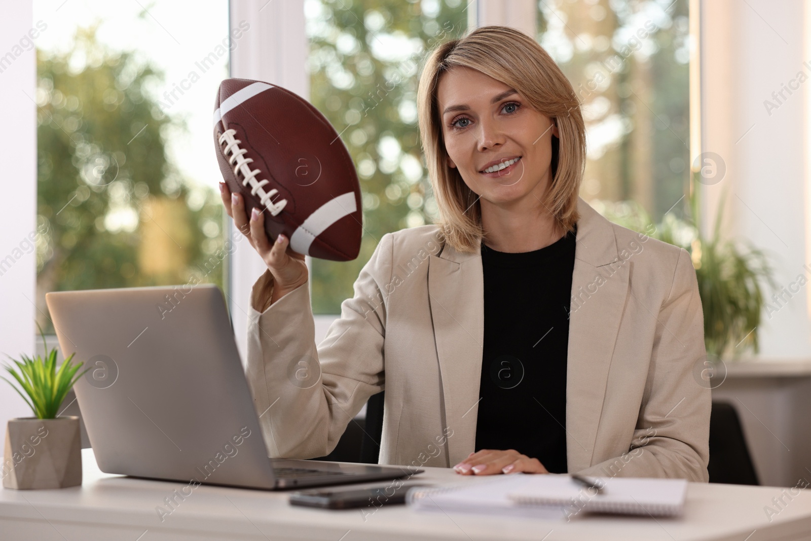 Photo of Smiling woman with american football ball at table in office