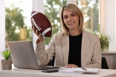 Smiling woman with american football ball at table in office