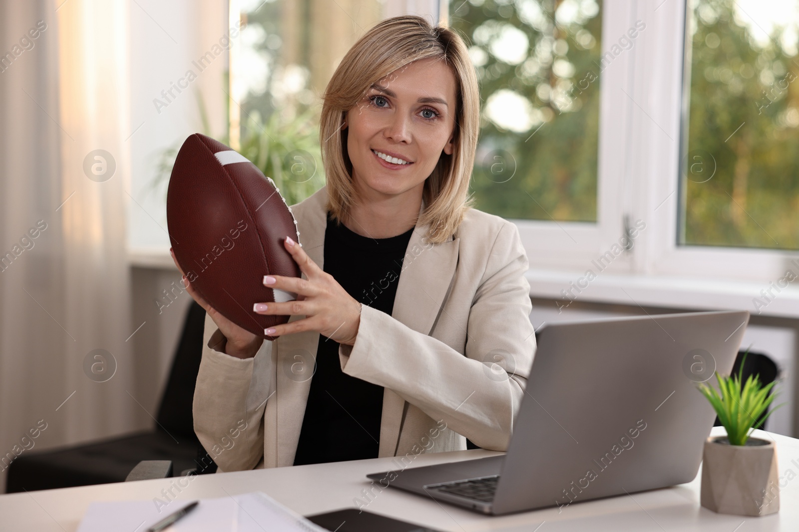 Photo of Smiling woman with american football ball at table in office