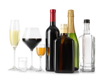 Bottles and glasses with different alcoholic drinks on white table against light background, space for text