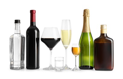 Bottles and glasses with different alcoholic drinks on white table against light background