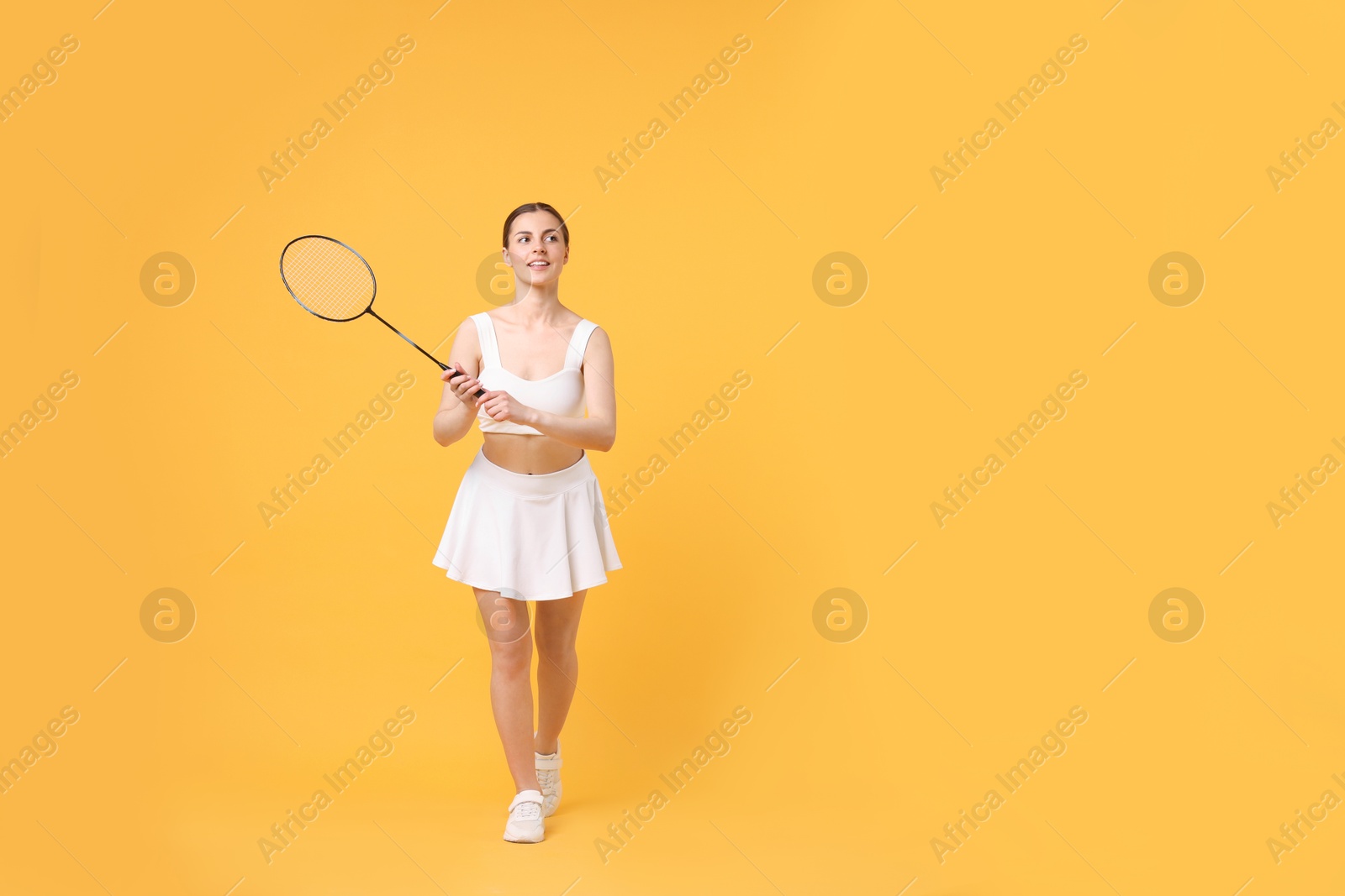 Photo of Young woman with badminton racket on orange background, space for text