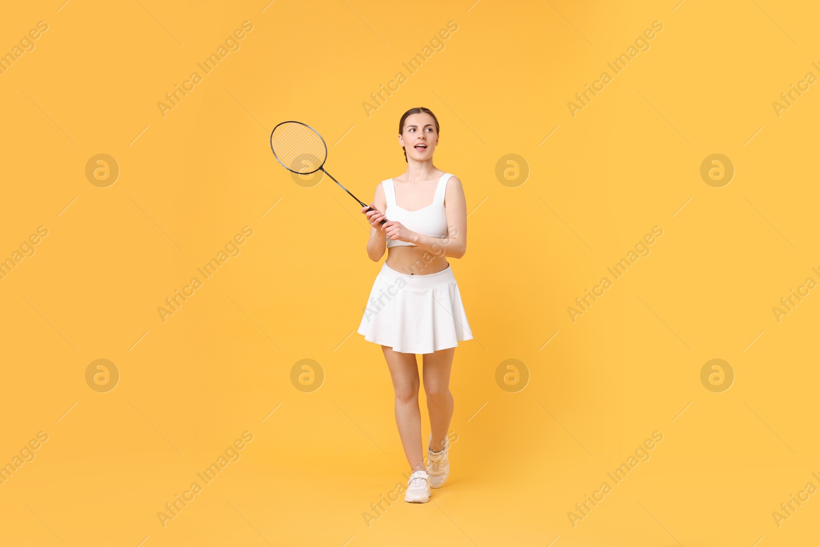 Photo of Young woman with badminton racket on orange background