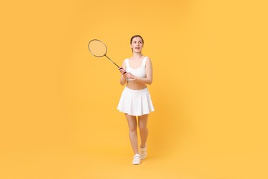 Young woman with badminton racket on orange background