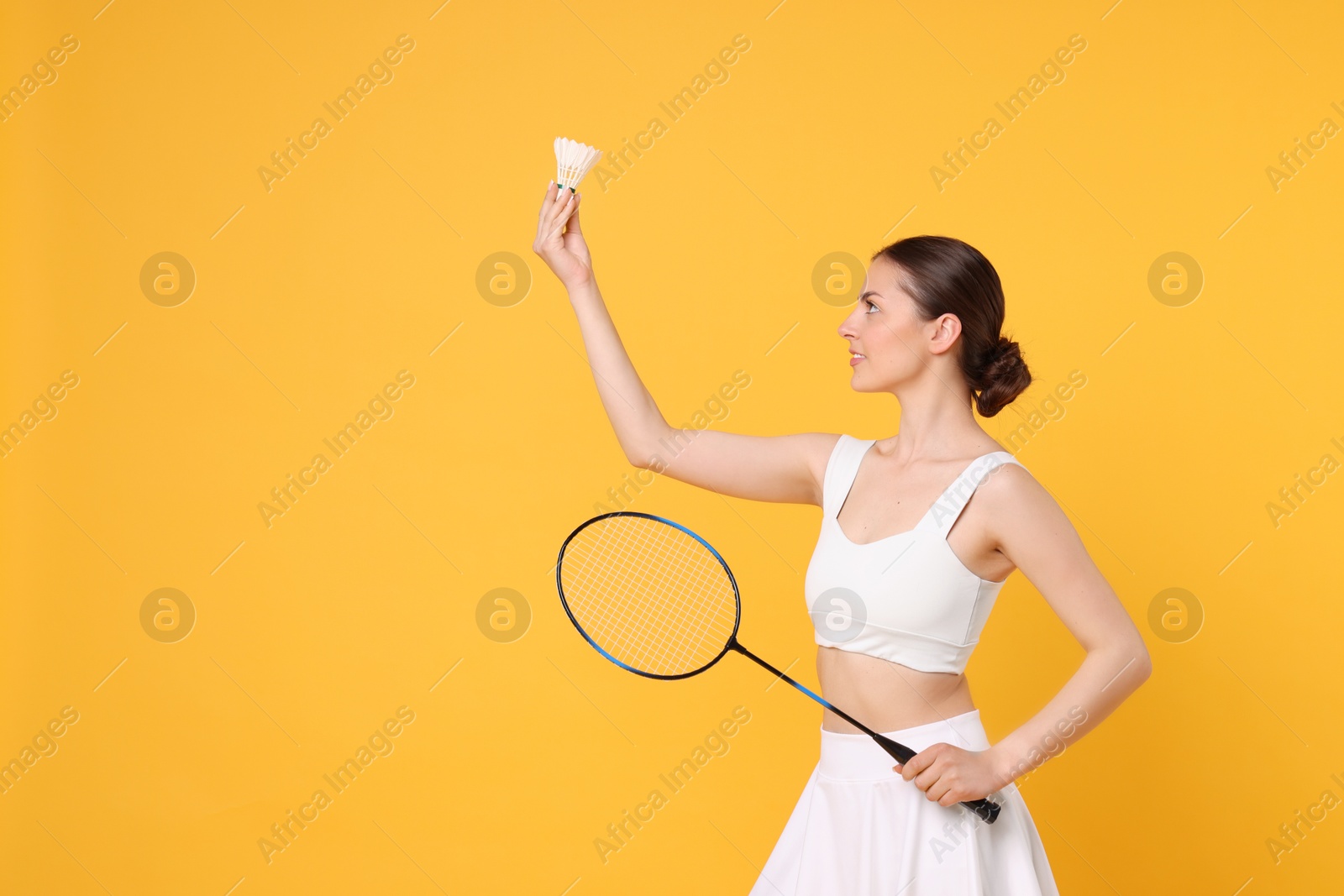 Photo of Young woman with badminton racket and shuttlecock on orange background, space for text