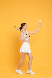 Photo of Young woman with badminton racket and shuttlecock on orange background