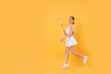 Young woman with badminton racket on orange background, space for text