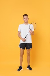 Young man with badminton racket on orange background