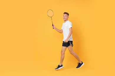 Photo of Young man with badminton racket on orange background, space for text