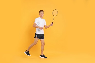 Young man with badminton racket on orange background, space for text