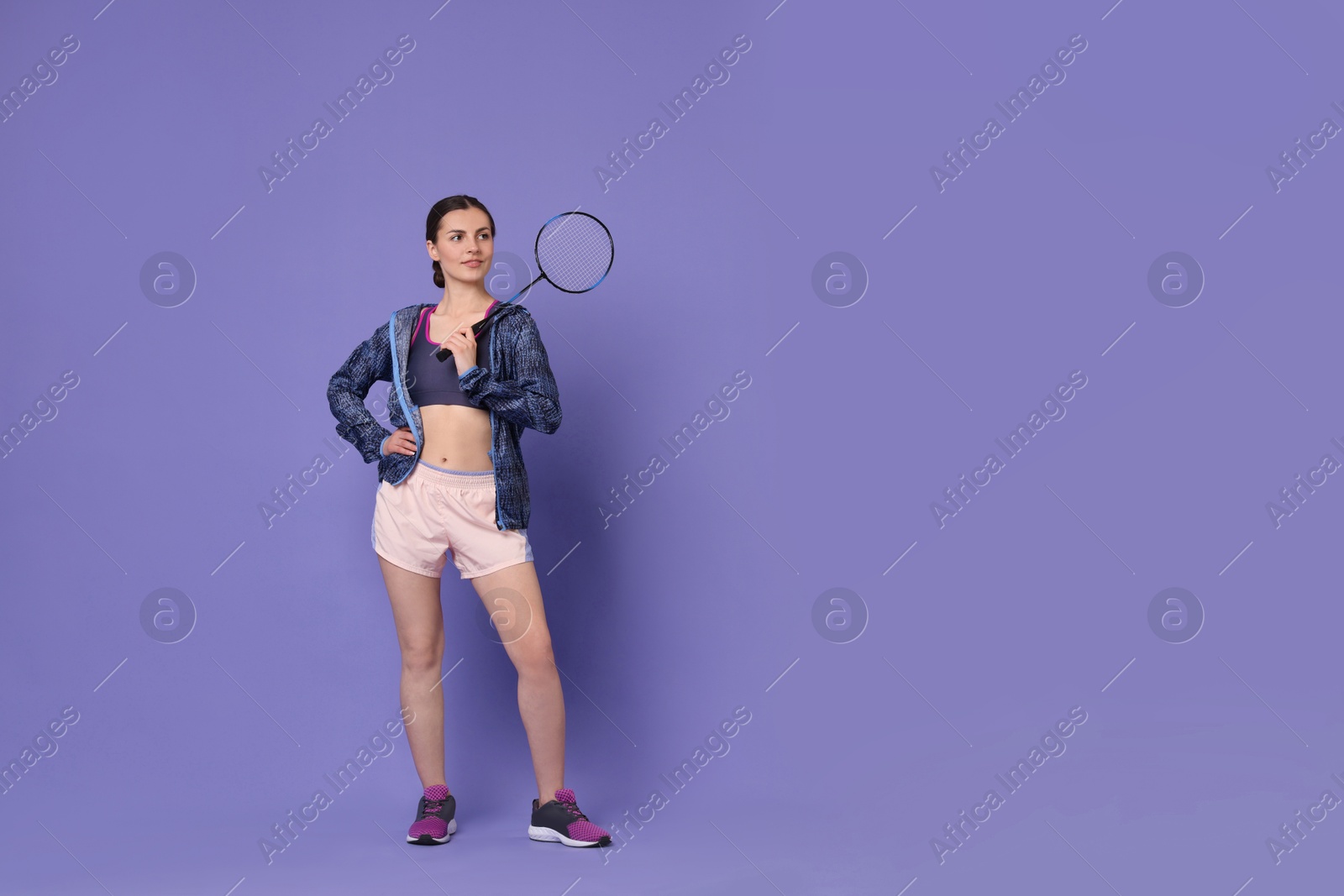Photo of Young woman with badminton racket on purple background, space for text