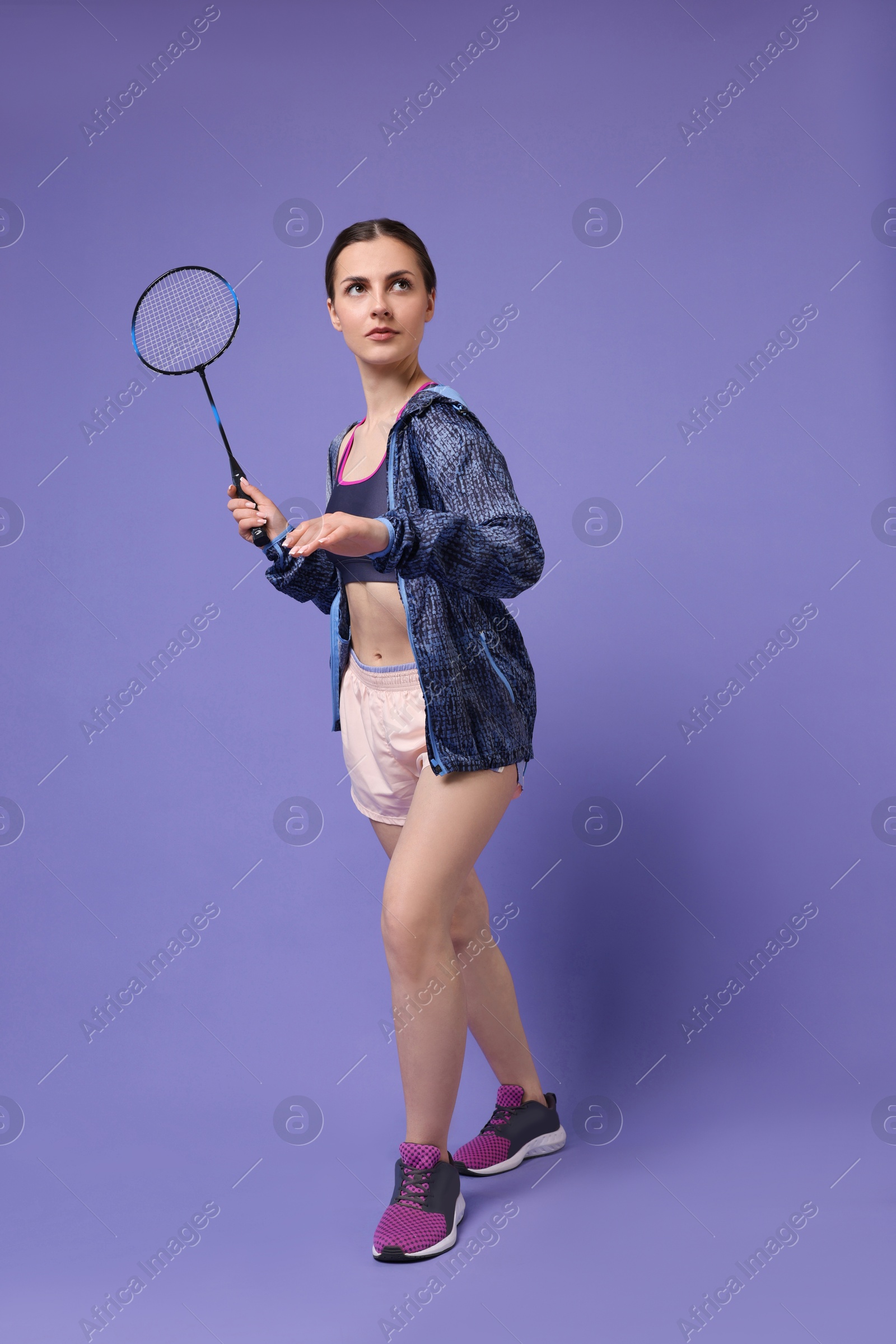 Photo of Young woman playing badminton with racket on purple background
