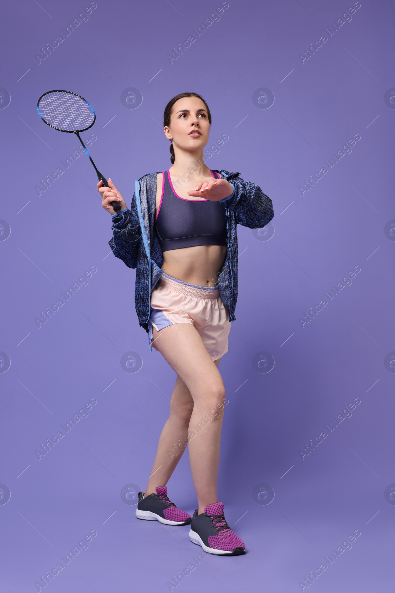 Photo of Young woman playing badminton with racket on purple background