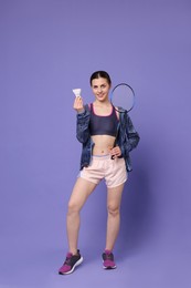 Young woman with badminton racket and shuttlecock on purple background