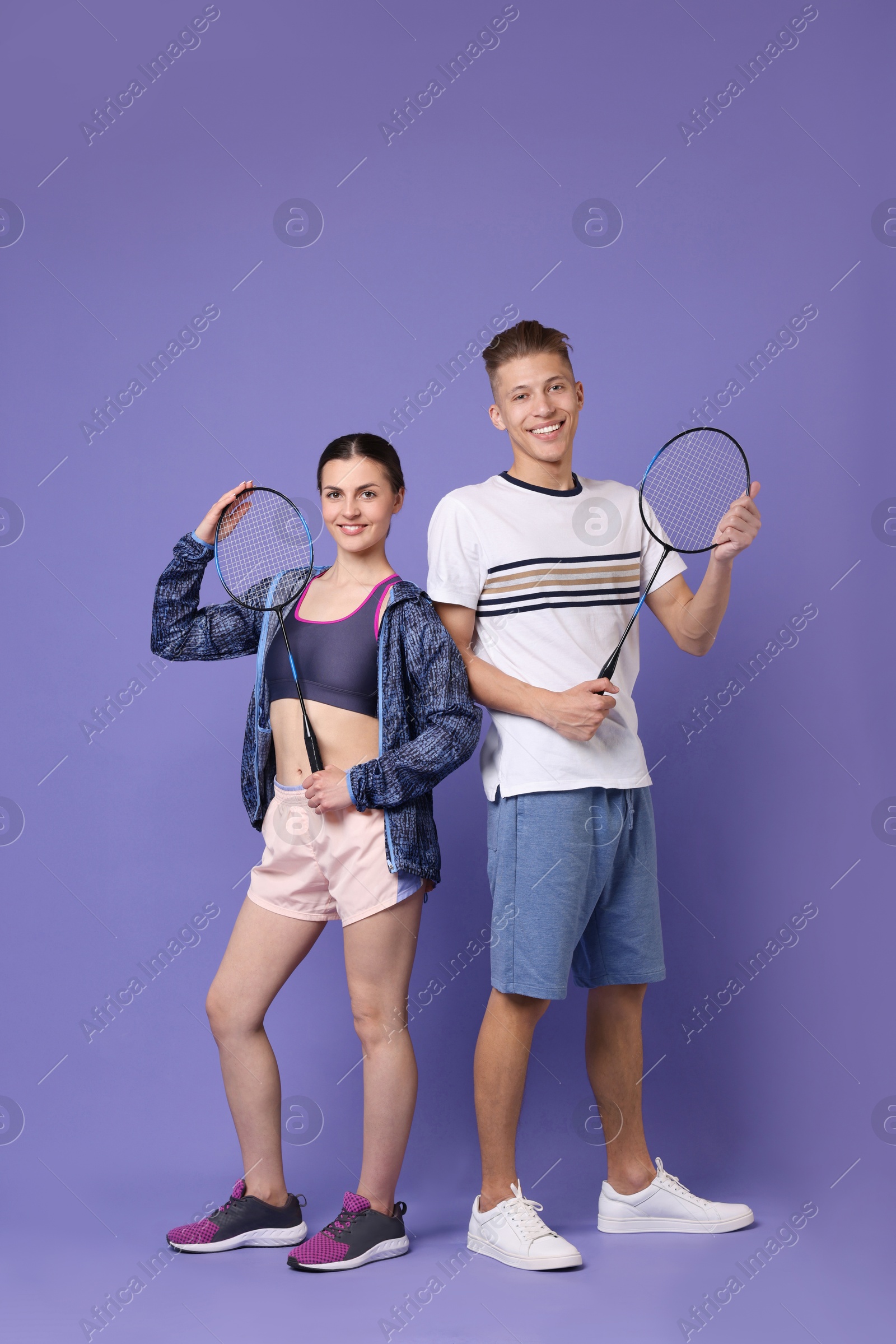 Photo of Young man and woman with badminton rackets on purple background