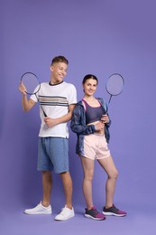 Young man and woman with badminton rackets on purple background