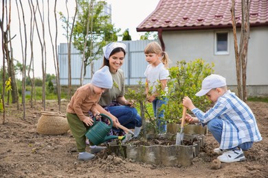 Mother and her children planting tree together in garden