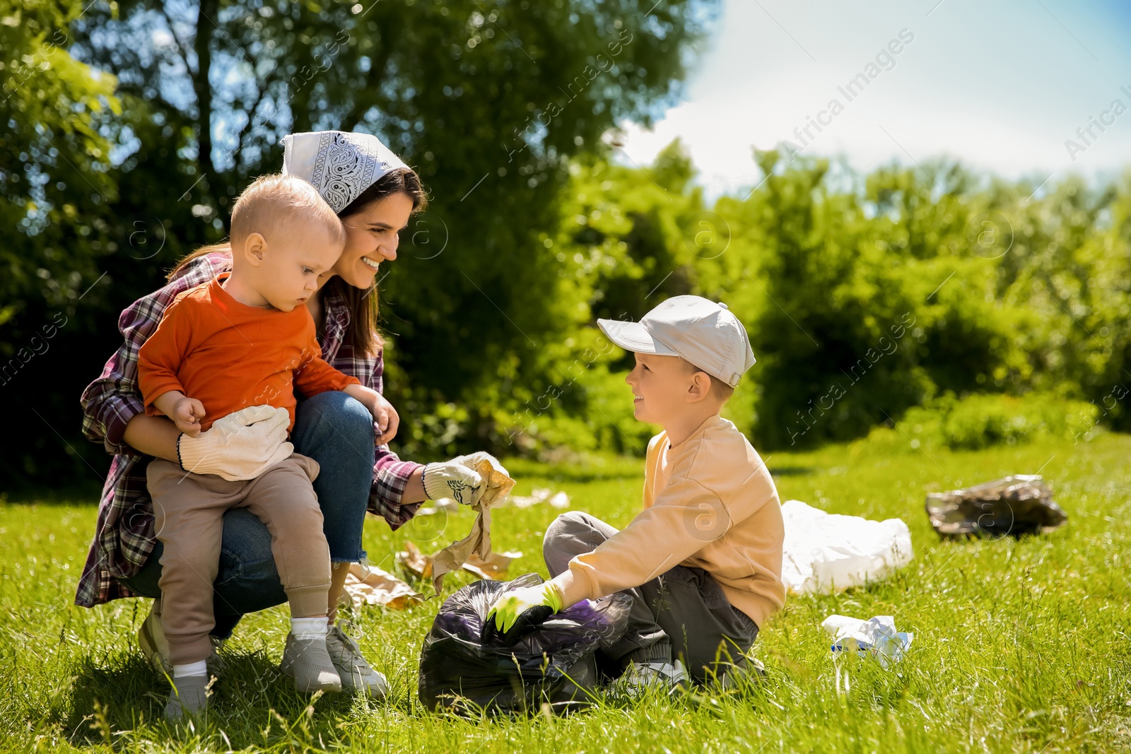 Photo of Mother and her children with plastic bags collecting garbage in park