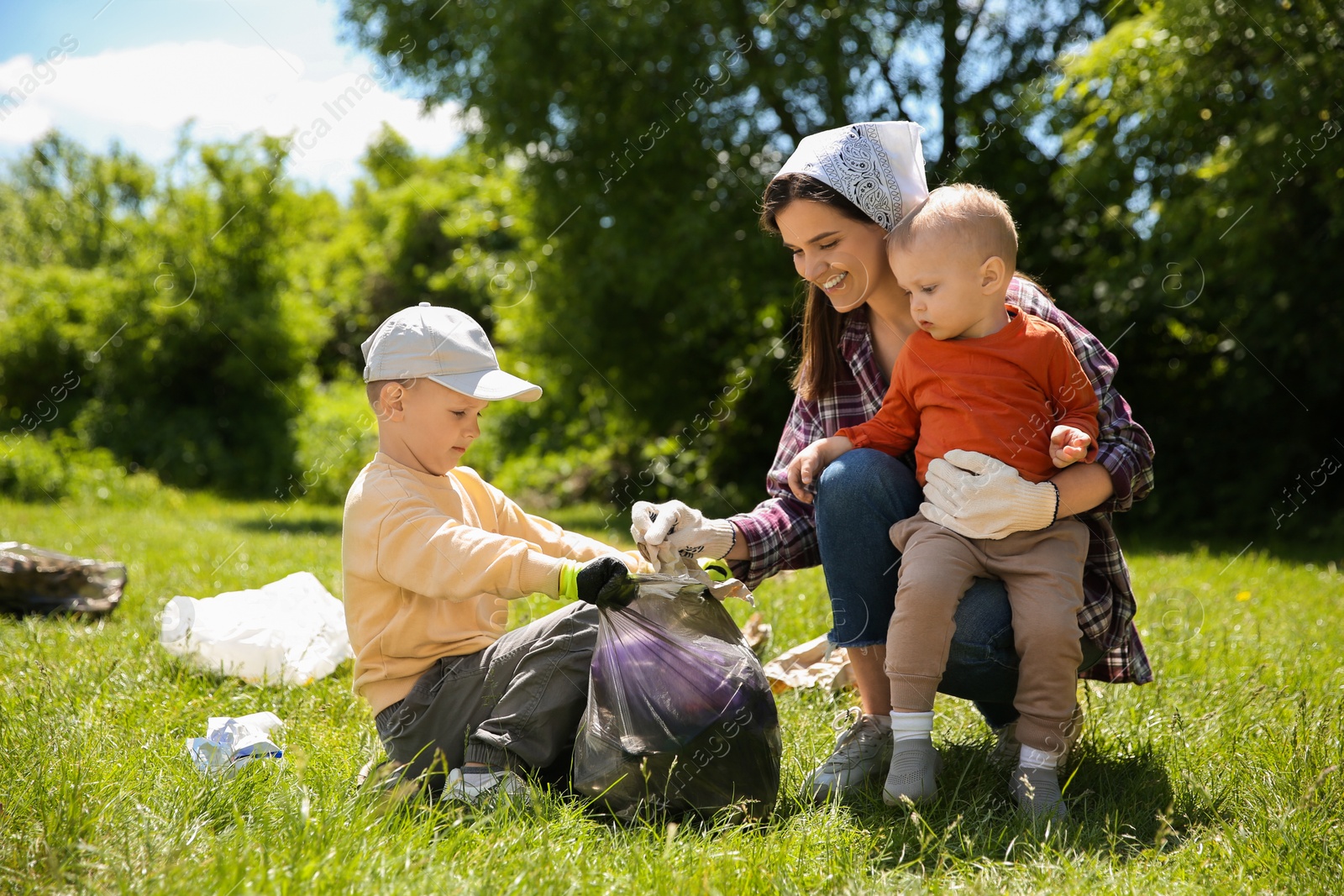 Photo of Mother and her children with plastic bags collecting garbage in park