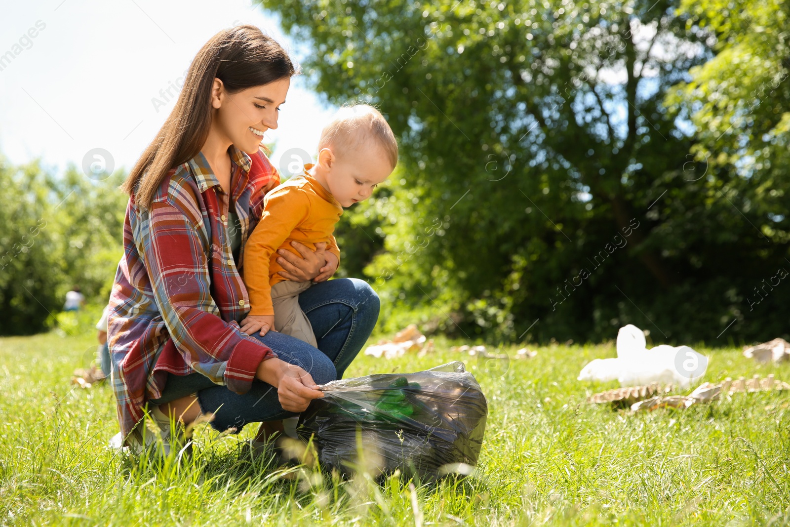 Photo of Mother and her son with plastic bag collecting garbage in park