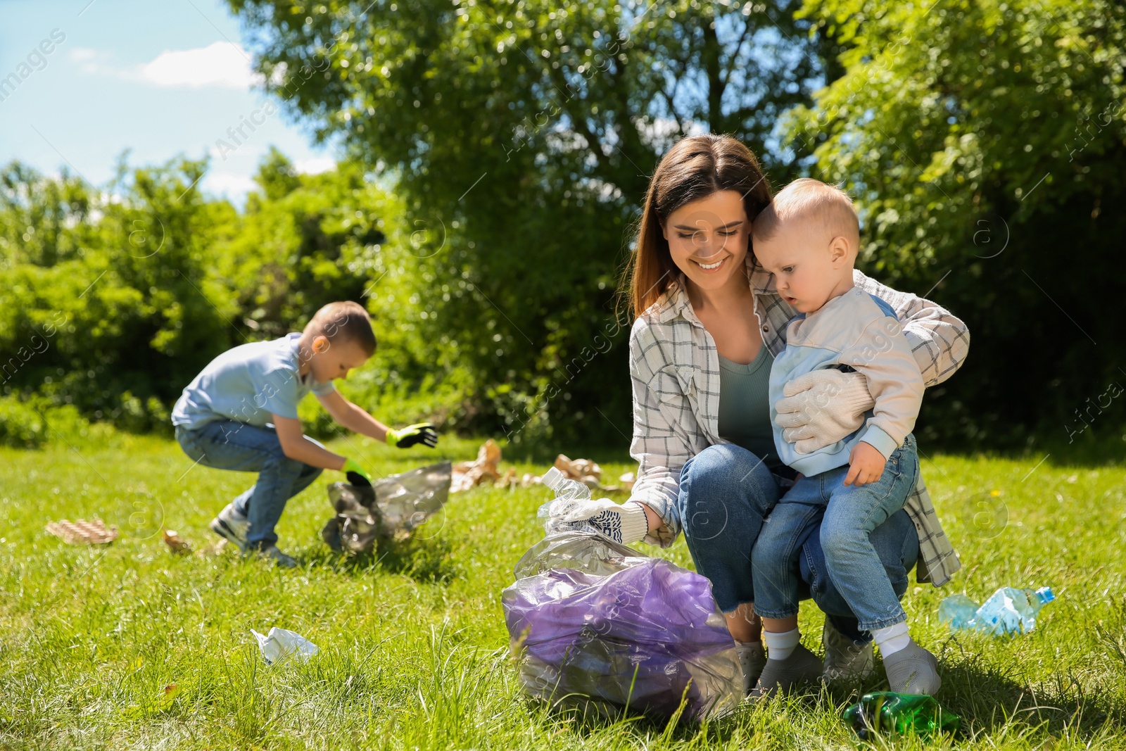 Photo of Mother and her children with plastic bags collecting garbage in park
