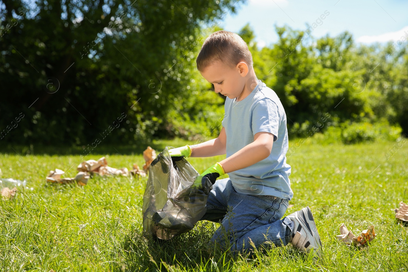 Photo of Little boy with plastic bag collecting garbage in park